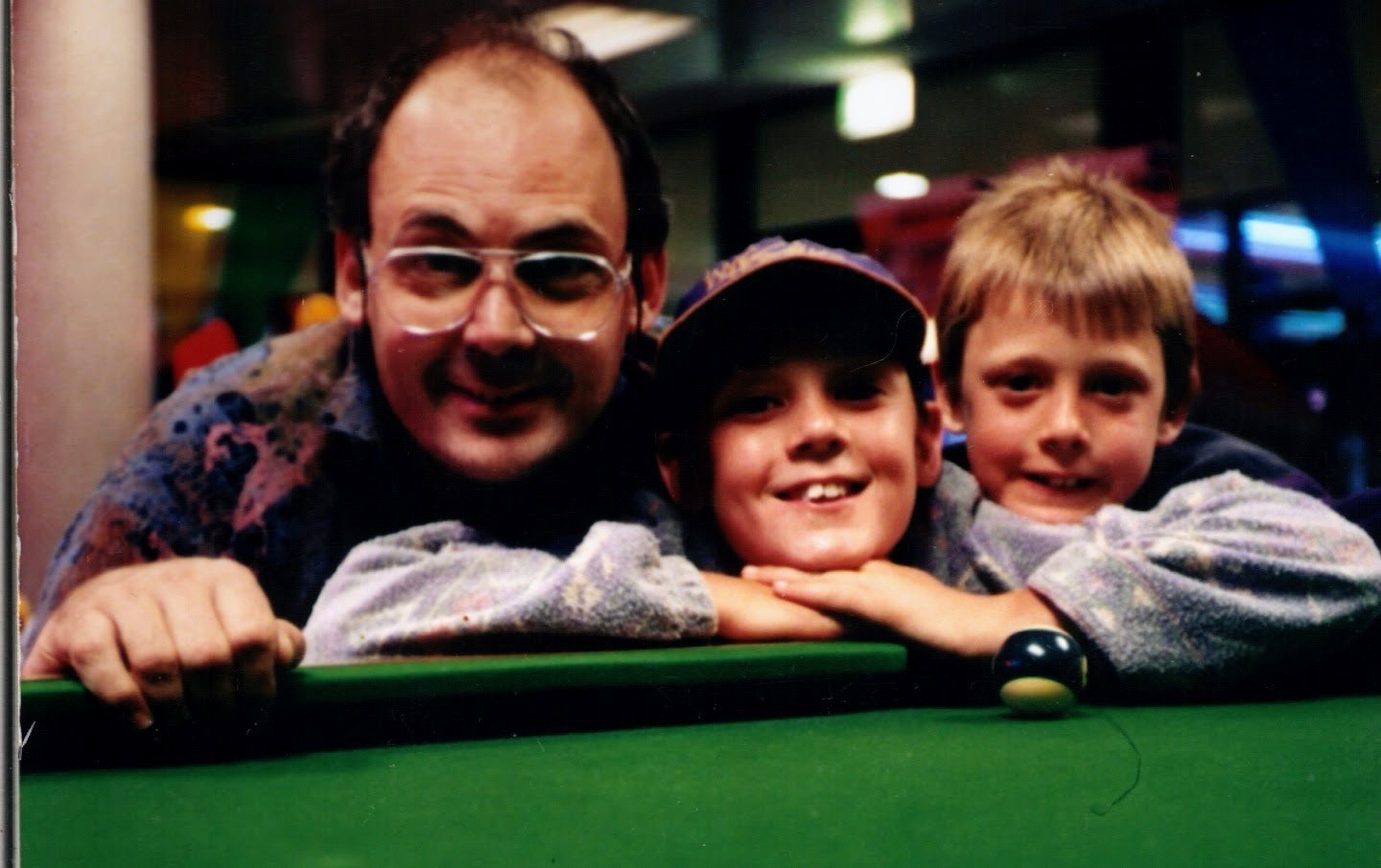 A man leaning over a pool table beside two boys