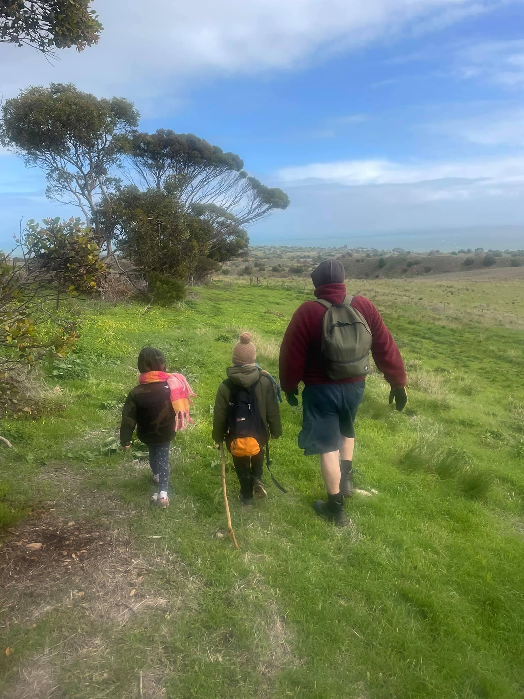 Martin walking with two children across a grassy coastal landscape, seen from behind