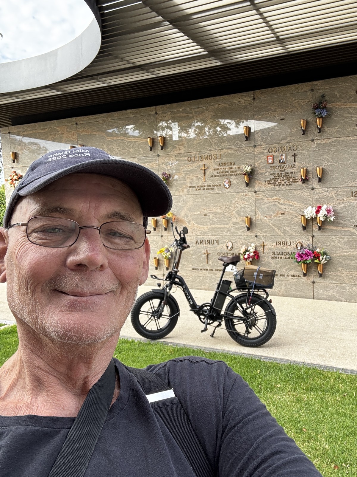 Martin in front of a memorial wall at Cheltenham Cemetery, with an e-bike behind him